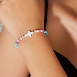 Close-up of colorful beaded bracelet featuring a white shell cross charm and gold accents