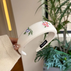 Detail of a white padded floral headband with delicate pink and blue flower embroidery