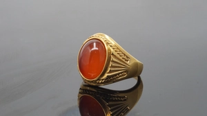Detail view of a vintage gold ring with a polished oval red agate stone and textured carving