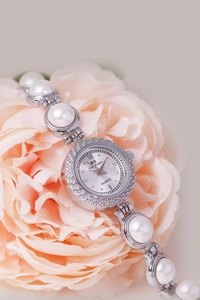 Elegant silver watch with white pearl bracelet band displayed on a soft pink peony