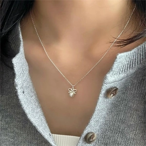 Close-up of bow knot pearl pendant necklace worn by a model on a soft background
