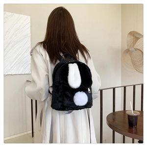 Close-up of black and white fuzzy backpack with bunny ears on model in a cozy setting