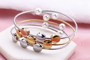 Detail of multi-layer steel cable bracelet with tri-color charms and white pearl accents