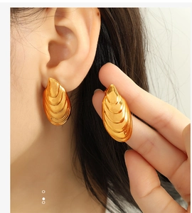 Detail of gold shell-patterned stainless steel earrings on model showing size and texture