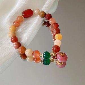 Detail eines Edelsteinarmbands mit 18 Karat vergoldetem Blumenanhänger auf Chiffon