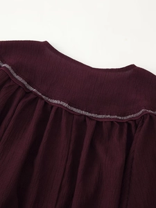 Close-up of dark burgundy linen blouse featuring white zigzag stitching and pleated texture