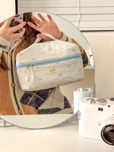 Detail of blue bow print on white quilted cosmetic bag with zipper and sturdy handle