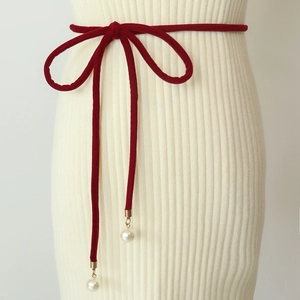 Detail of red velvet waist belt with pearl charms tied in a bow on a white knit dress