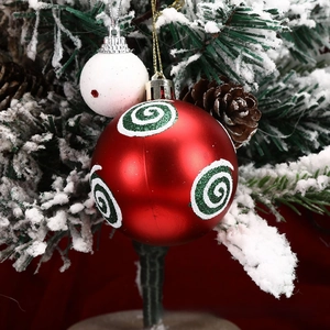 Close-up of red matte Christmas ball with green glitter spiral on snowy pine tree branch