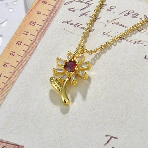 Detailed macro view of a golden sunflower necklace pendant with red and clear zircon stones