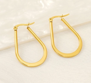 Detail showing polished gold teardrop earrings on textured fabric and ceramic prop