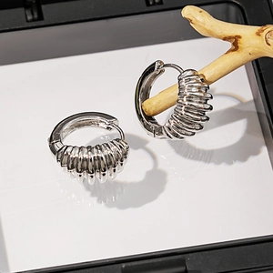 Boucle d'oreille créole torsadée argentée suspendue sur support en bois naturel