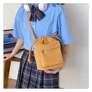 Detail of yellow corduroy drawstring bucket bag worn over a blue casual sweatshirt