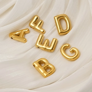 Polished 18K gold balloon letter pendants with metallic crinkle texture on white fabric