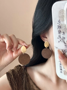 Detail of vintage geometric wood and gold metal earrings worn by model in a soft studio light