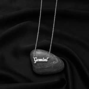 Macro shot of silver Gemini constellation necklace pendant on gray river stone