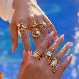 Close-up of stacked 18K gold-plated irregular zircon rings on model's hand by the pool
