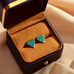 Macro view of heart-shaped malachite earrings with gold borders in a velvet box