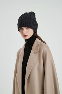Detail of a women's black chunky knit beanie paired with a classic camel wool coat