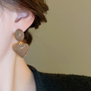Macro shot of mocha enamel heart drop earrings with gold edges on a model's ear
