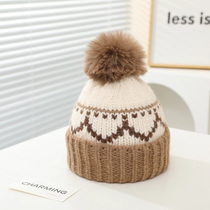 Detailansicht von Herz-Jacquard-Muster und flauschigem Bommel auf Winterstrickmütze