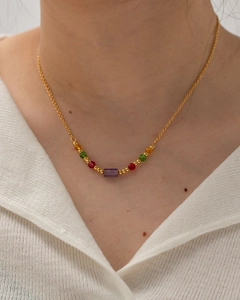 Close-up of a gold necklace with colorful beads and a purple rectangular stone on a model