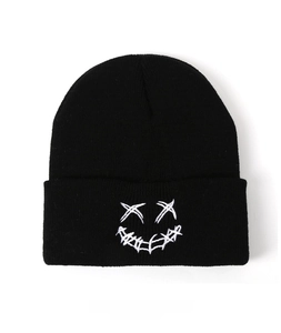 Close-up of black knit beanie featuring white embroidered stitched smiley face pattern