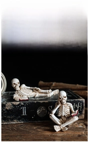 Close-up of gothic skeleton resin figurines reading books on a dark wooden surface