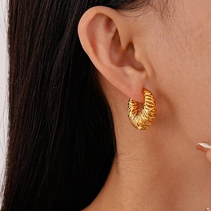 Close-up of a woman wearing gold twisted croissant hoop earrings with a woven texture
