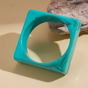 Detailed shot of square turquoise marble resin bangle leaning on a textured stone prop