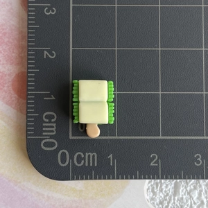 Vue détaillée d'une breloque miniature en résine de 1,5 cm sur une règle de mesure noire