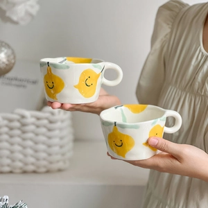 Detail of hand-painted ceramic mugs with yellow pear patterns held by two hands