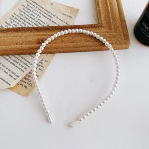 Detail of white faux pearls arranged on a slim metal headband with vintage book decor