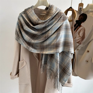 Detailed view of blue and brown plaid scarf with fringe on a beige coat texture