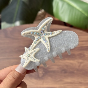 Sparkling starfish hair claw clip with rhinestones held in hand over a wooden background