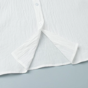 Close-up of white pleated shirt hem with button placket and textured seersucker fabric