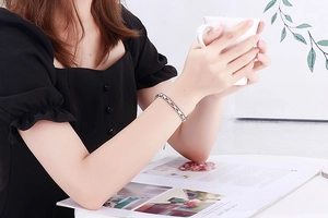 Silver metal chain bracelet shown on a wrist while holding a white coffee cup