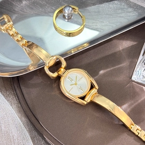 Detail of vintage gold-tone oval quartz watch on a dark surface with a pearl ring