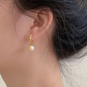 Close-up of minimalist gold drop earrings with round white pearls on model's ear