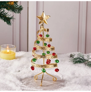 Mini gold metal spiral Christmas tree with colorful bells and top star on snowy background