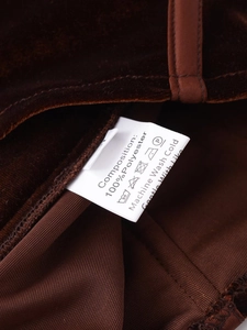 Nahaufnahme des Waschetiketts mit 100% Polyester auf braunem Samtstoff des Kleidungsstücks