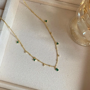 Detailed macro view of gold-plated necklace with green gemstone charms and white zircon stones