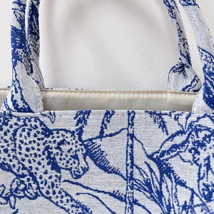 Detailed embroidery of leopard and tropical leaf patterns on a blue jacquard tote bag