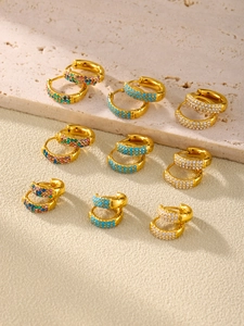 Detail of gold earrings with turquoise beads and colorful zircon on marble surface