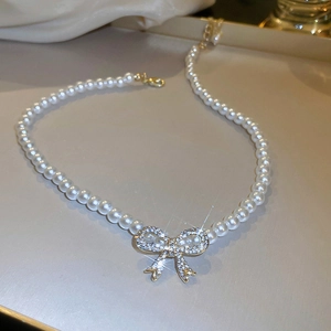 Macro detail of white pearl necklace featuring a sparkling gold bow pendant with rhinestones