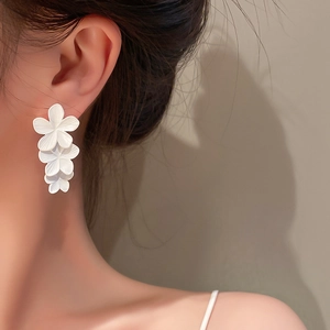 Detailed close-up of triple matte white flower drop earrings worn for elegant style