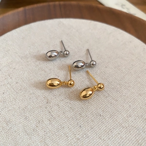 Détail macro de boucles d'oreilles goutte plaquées or 18k et argent sur plateau bois