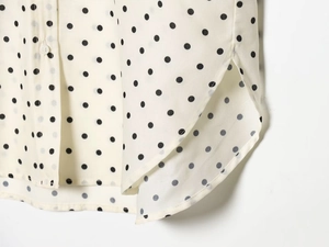Detail of retro polka dot shirt hem showing button closure and side slit on cream fabric