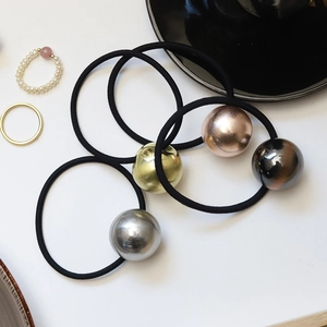 Minimalist elastic hair ties with textured metallic gold spheres on a white ceramic plate