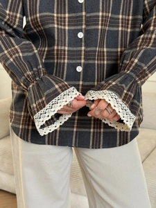 Detailed view of white lace trim cuffs on a dark grey plaid long-sleeve casual shirt